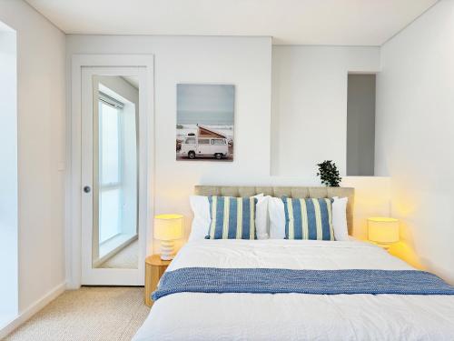 a white bedroom with a bed with blue and white pillows at Casa Lumi Walk to Marina & Beach in Shellharbour