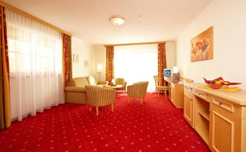 a room with a red carpet and a living room with a table at Alpenhotel Rieger in Mittenwald