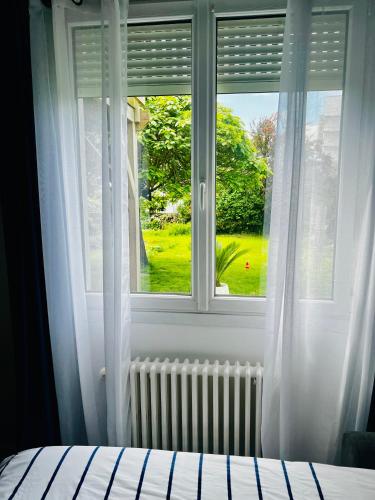 a bedroom window with a view of a green yard at Chambre Privée chez L' Habitant in Trignac