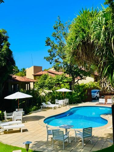 a swimming pool with chairs and tables and umbrellas at Pousada Coisa e Tao in Arraial d'Ajuda