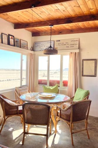 a dining room with a table and chairs and windows at Wlotzkasbaken, Barefoot Self-catering in Wlotzkasbaken