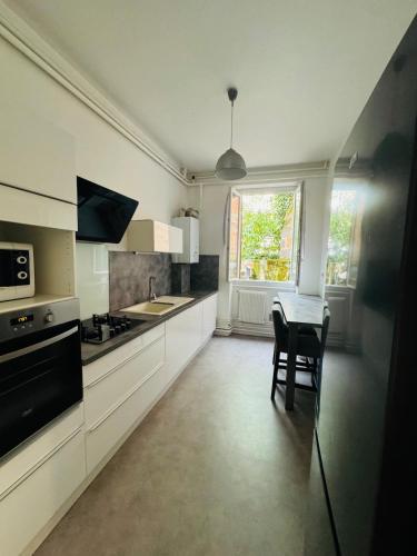 une cuisine avec des armoires blanches, une table et une fenêtre dans l'établissement Grand appartement hyper-centre, à Clermont-Ferrand