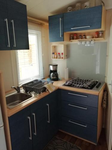 - une cuisine avec des placards bleus, une cuisinière et un évier dans l'établissement mobil home chez ANIK & ALAIN, à La Roque-dʼAnthéron