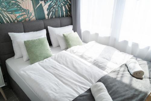 a white bed with white sheets and green pillows at REMZ Apartments & Wellness in Dorog
