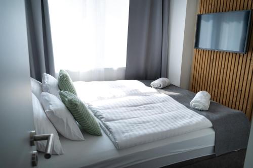 a bedroom with a white bed with pillows and a television at REMZ Apartments & Wellness in Dorog