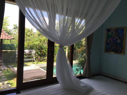 a bedroom with a bed and a window with curtains at Ratna Villa in Ubud