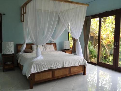 a bedroom with a bed with white sheets and curtains at Ratna Villa in Ubud