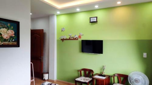 a room with a green wall with chairs and a tv at NEST House in Ấp Kim Thạch