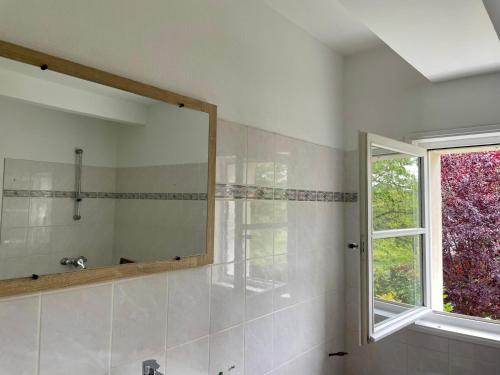La salle de bains est pourvue d'un grand miroir et d'une fenêtre. dans l'établissement Maison Mirande- Grande maison de campagne familiale entre mer et montagne tout confort très bien équipée, à Guinarthe-Parenties
