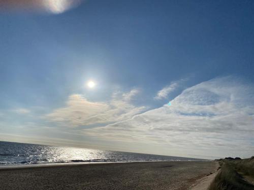 a beach with the sun in the sky and the ocean at Happydaze Caravan in Bacton