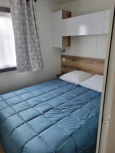 Cette chambre dispose d'un grand lit bleu et d'une fenêtre. dans l'établissement Mobilhome neuf 3 chambres Oléron, à Saint-Denis-dʼOléron