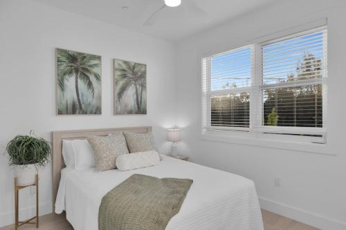 a white bedroom with a bed and two windows at Hooked on Islamorada Oceanfront Townhome, Private Dock, Pool in Islamorada