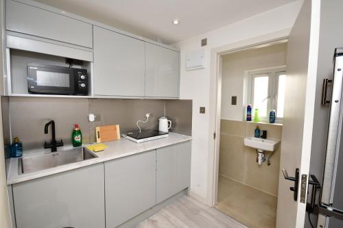 a kitchen with white cabinets and a sink and a microwave at Comfortable bedrooms in Kingston in Kingston upon Thames