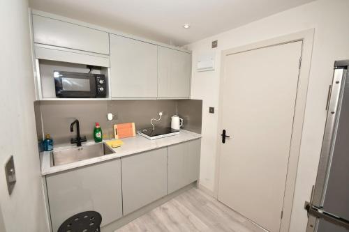 a kitchen with white cabinets and a sink and a door at Comfortable bedrooms in Kingston in Kingston upon Thames