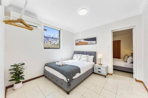 a white bedroom with a bed and a plant at Cheerful Two Bedroom house in Sydney