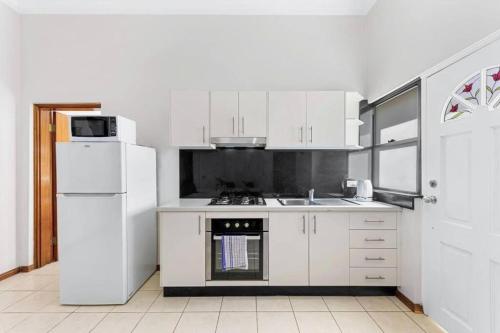 a kitchen with white cabinets and a white refrigerator at Cheerful Two Bedroom house in Sydney