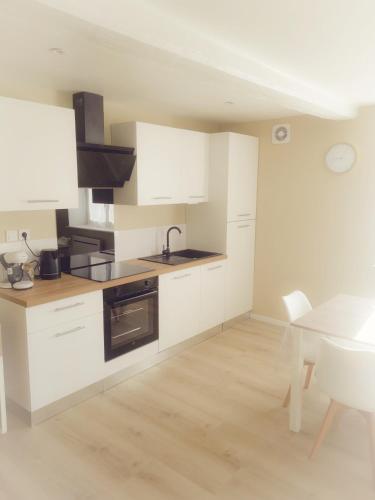 - une cuisine avec des placards blancs, un évier et une table dans l'établissement La Pluméria Appartement 2 chambres, à Saint-Germain-Lespinasse