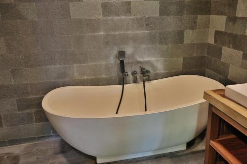 a bath tub in a bathroom with a stone wall at Umah D Meranggi in Banjarangkan