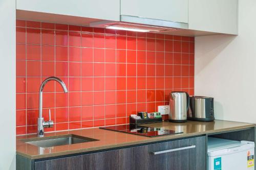 a kitchen with a sink and a red tiled wall at Comfort Apartments Box Hill in Box Hill