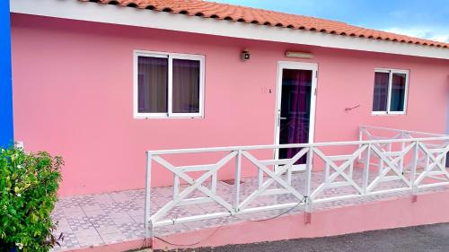 a pink house with a white railing in front of it at Central - Gated - 2 Bedrooms - Near Beaches in Julianadorp