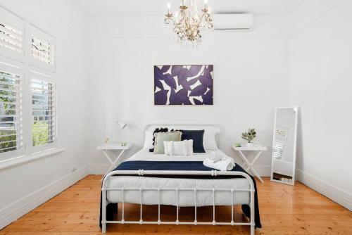 a bed in a white room with a chandelier at Orontes Cottage - Geelong Rippleside Retreat in Geelong