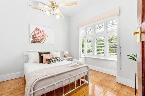 a white bedroom with a bed and a ceiling fan at Orontes Cottage - Geelong Rippleside Retreat in Geelong