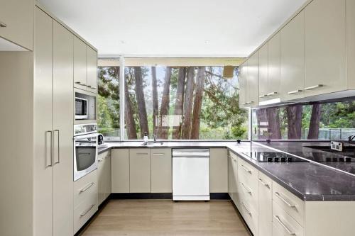Una cocina con gabinetes blancos y una ventana grande. en Quaint Queen Room - Central Location at Pymble - Shared Bathroom, en Pymble