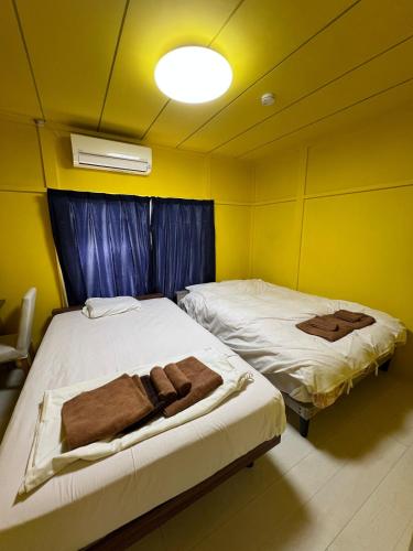 Dos camas en una habitación con paredes amarillas. en ホテルペナ101, en Tokio