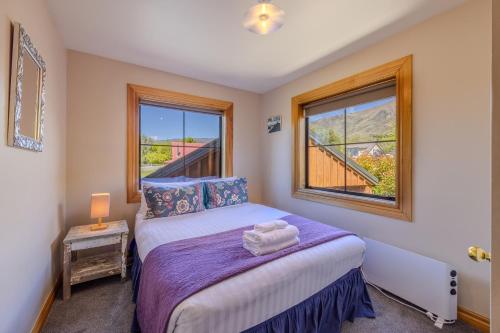 a small bedroom with a bed and two windows at Minaret Cabin - 3 bedroom home in Wanaka