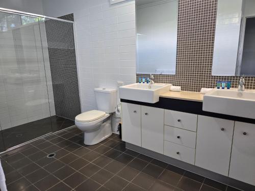 a bathroom with a toilet and two sinks and a shower at Quarterdecks Retreat in Hervey Bay