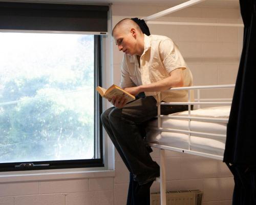 a man sitting on a bunk bed reading a book at Little Drifter North Melbourne in Melbourne
