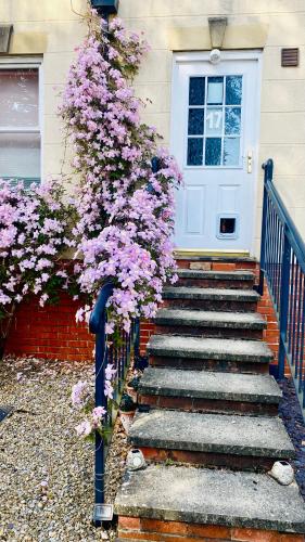 a house with a white door and purple flowers at Modern ground floor apartment with free parking very near centre in Ripon