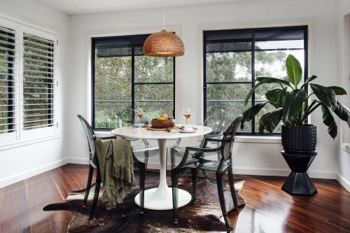 a dining room with a white table and chairs and windows at Jungle Cubby by Coast Hosting in Terrigal