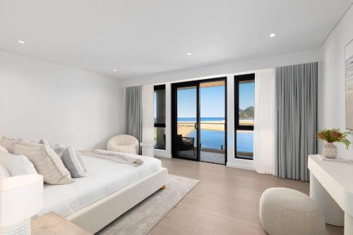 a white bedroom with a bed and a view of the ocean at Maggie's by Coast Hosting in North Avoca