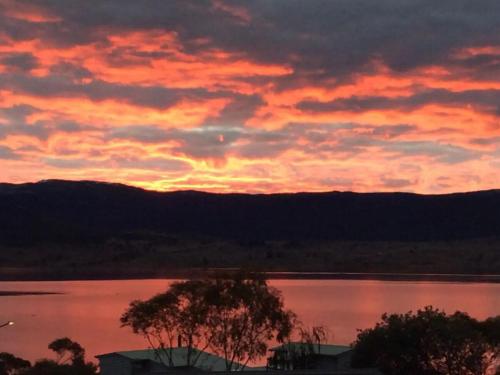 a sunset over a lake with a tree in the foreground at Flow Rider #6 in Jindabyne