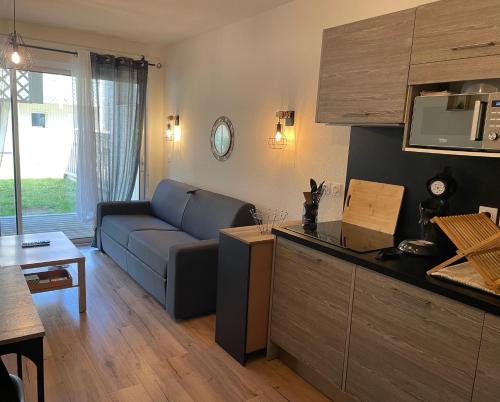 a living room with a blue couch and a kitchen at Appartement 200m de l'océan avec piscine extérieure in Mimizan