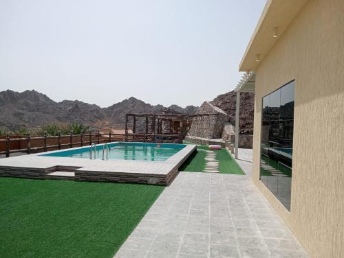 a swimming pool with green grass next to a building at Hatta Guest house Resort in Būbādī