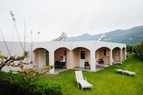 a white building with chairs and tables in the grass at Finikas Apartments in Plakias