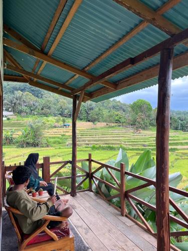 two people sitting in chairs on a porch with a view of a field at Ikua Tanjuang in Situjuhbatul