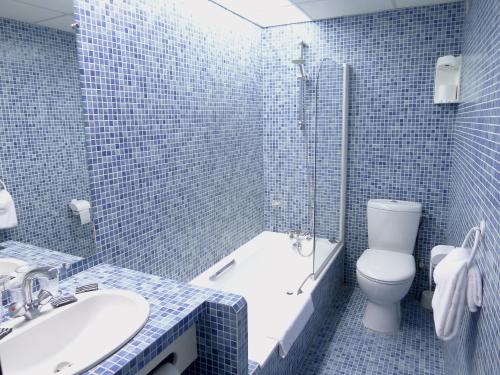 La salle de bains est pourvue de carrelage bleu, de toilettes et d'un lavabo. dans l'établissement Hôtel du Sablar, à Mont-de-Marsan