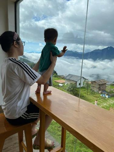 a woman holding a child sitting on a table looking out a window at 1579 Homestay Sapa - Venuestay in Sa Pa