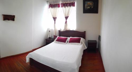 a bedroom with a white bed with red pillows and a window at Hotel Alcayata Colonial in Popayan