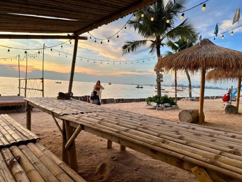a woman walking on a beach with a wooden bench at Golden Dragon Beach Resort Pattaya (Bang Lamung) in Ban Rong Po
