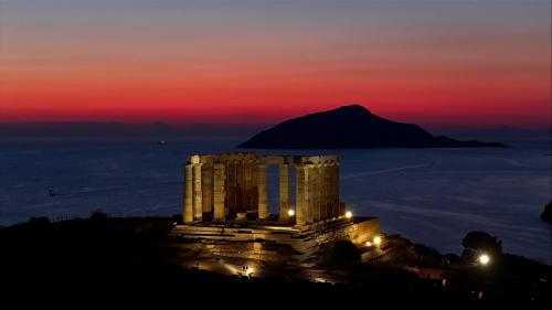 a temple with a mountain in the background at sunset at Athenian Lofts in Athens