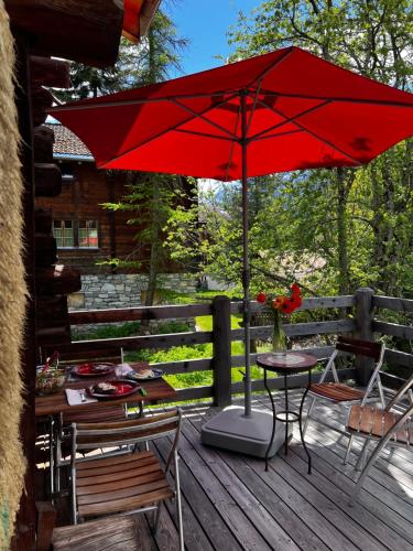 a red umbrella on a deck with a table and chairs at Grange de Fonville - Evolène - Valais in Evolène