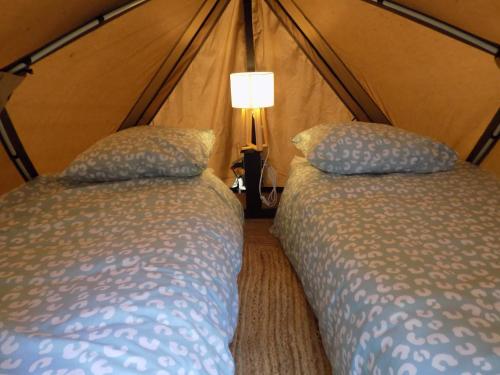 a bedroom with two beds and a lamp in a tent at Tente familiale au bord de l'eau in Le Vigeant