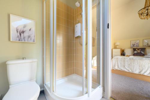a bathroom with a shower with a toilet and a bed at Cosy Cotswold Lodge by Your Home Here - SUMMER SALE for 3 PLUS NIGHTS - ideal for families with log-burner, spa, private parking, EV recharging and heated swimming pools in Ashton Keynes