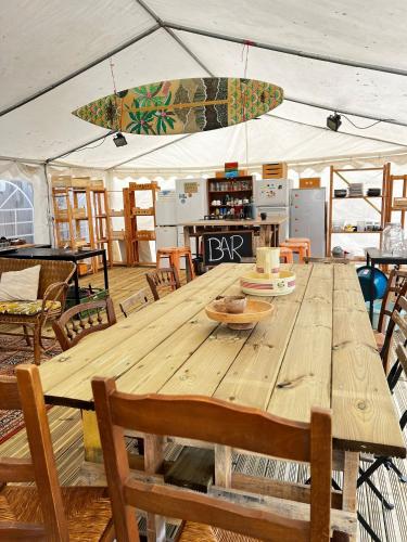une grande table en bois avec des chaises et une planche de surf dans l'établissement Glamping Spot - La Flotte en Ré, à La Flotte