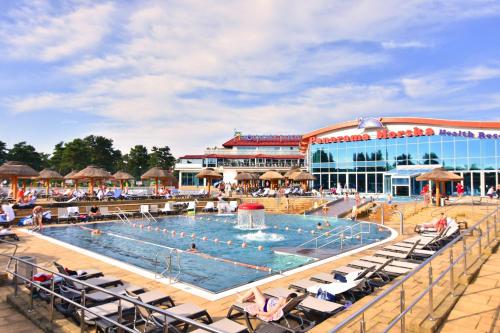 a pool with people sitting in chairs in front of a building at Willa Biały Dom - Aquapark Panorama Morska All Inclusive in Jarosławiec