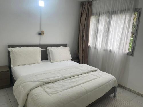 a bedroom with a bed with white sheets and a window at Appartement T3 in Abidjan